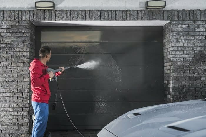 Garage Gate Pressure Washing by Caucasian Home Owner in His 30s. House Maintenance. Keeping the Place Clean. how to paint a garage door