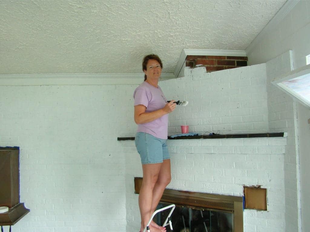 A woman painting a brick wall around a fireplace