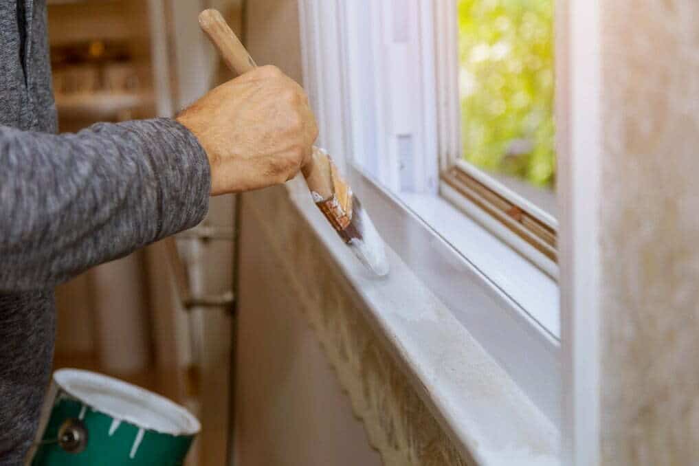 A man painting around the trim of his windows 